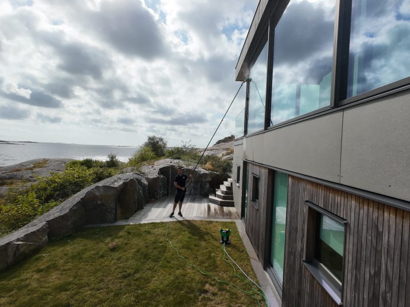 Fönsterputsare på väg längs en villa med stora glaspartier