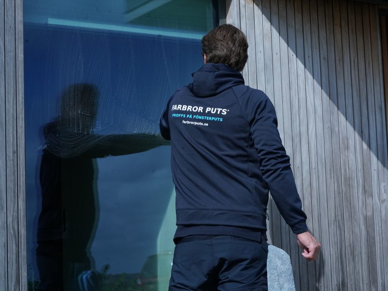 Farbror Puts handputsar ett fönster på en villa med träfasad