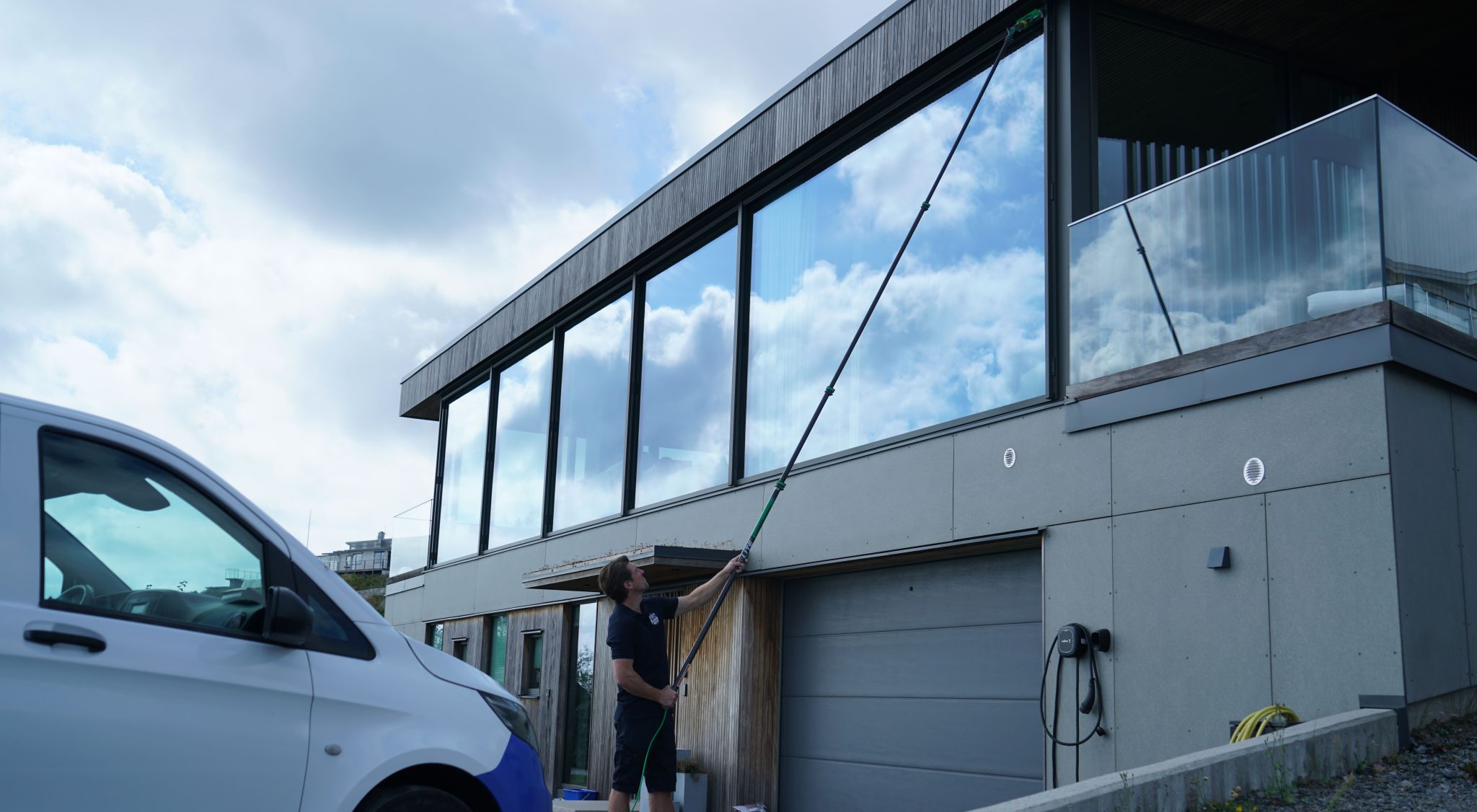 Fönsterputs vid en villa med stora glaspartier och servicebil